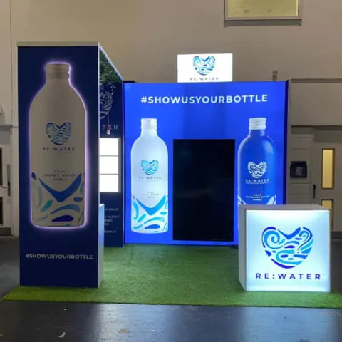 Rewater exhibitioon stand - lightbox back wall, with a bridge to a front wall holding a 3d bottle and backlit front counter